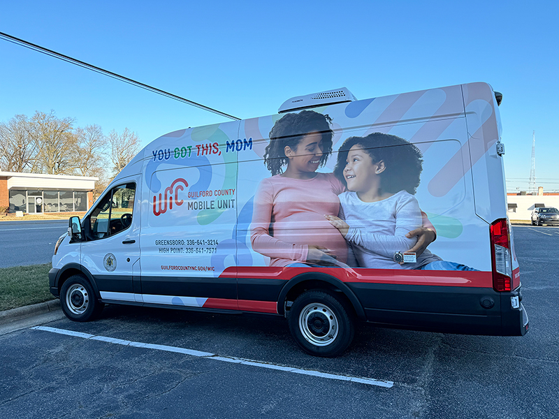 WIC mobile unit with smiling mother and daughter on the side.